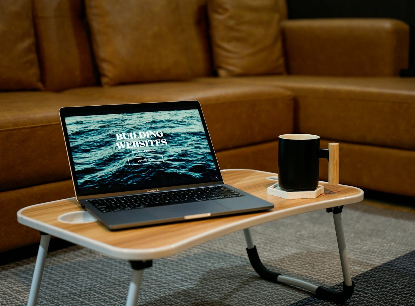 Computer portatile su un tavolino da letto con un sito web di design e una tazza di caffè.